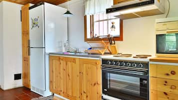 Cocina compacta con armarios de madera, horno empotrado, microondas y techo de madera.