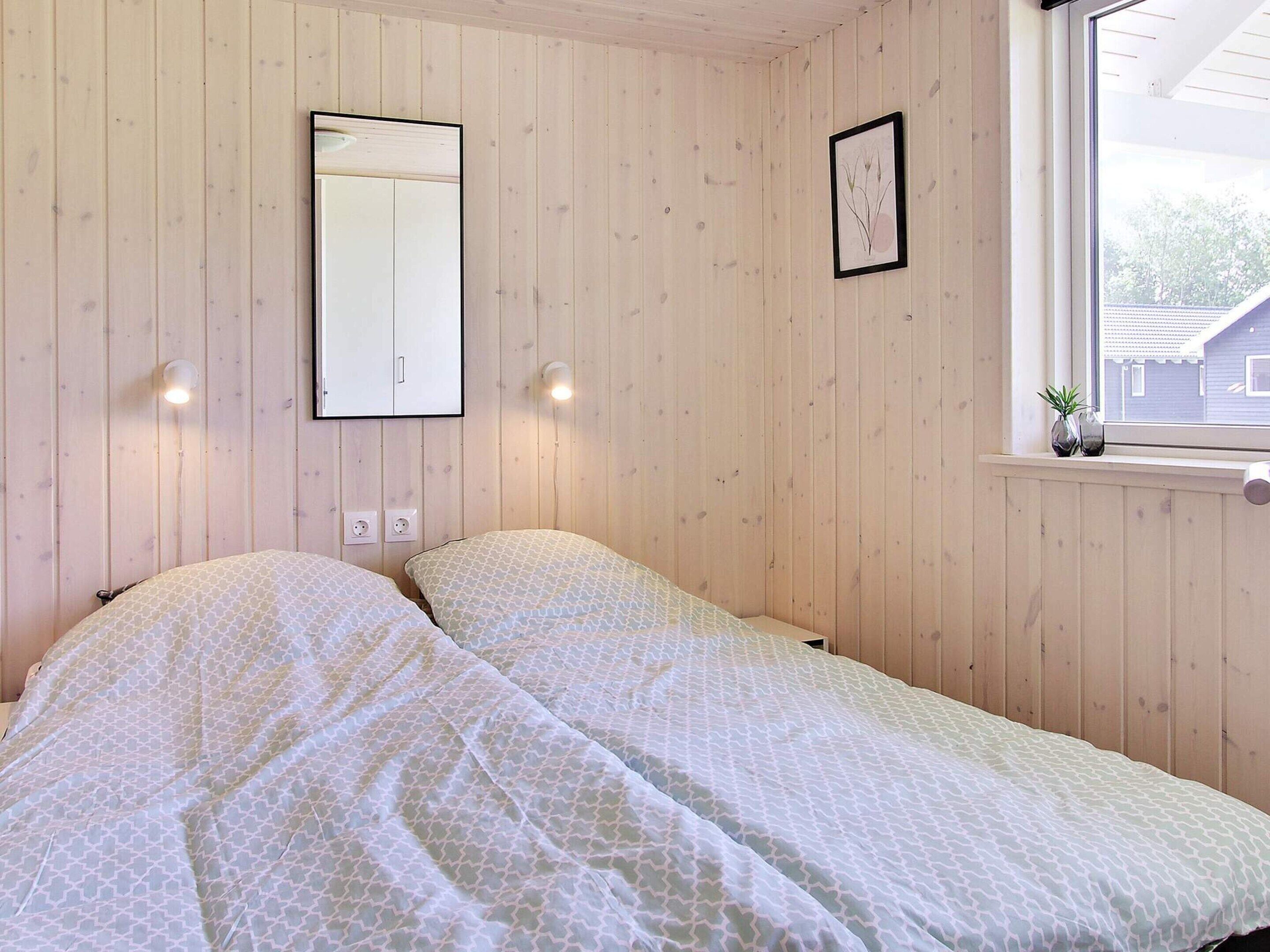 A room with two beds, wooden walls, a window with a view, a mirror, and a framed botanical print.
