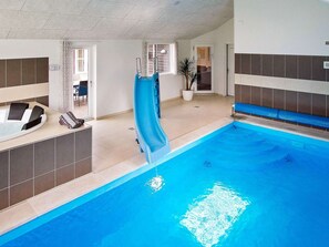 An indoor swimming pool with a slide, a hot tub, and a seating area with a view of the outdoors.