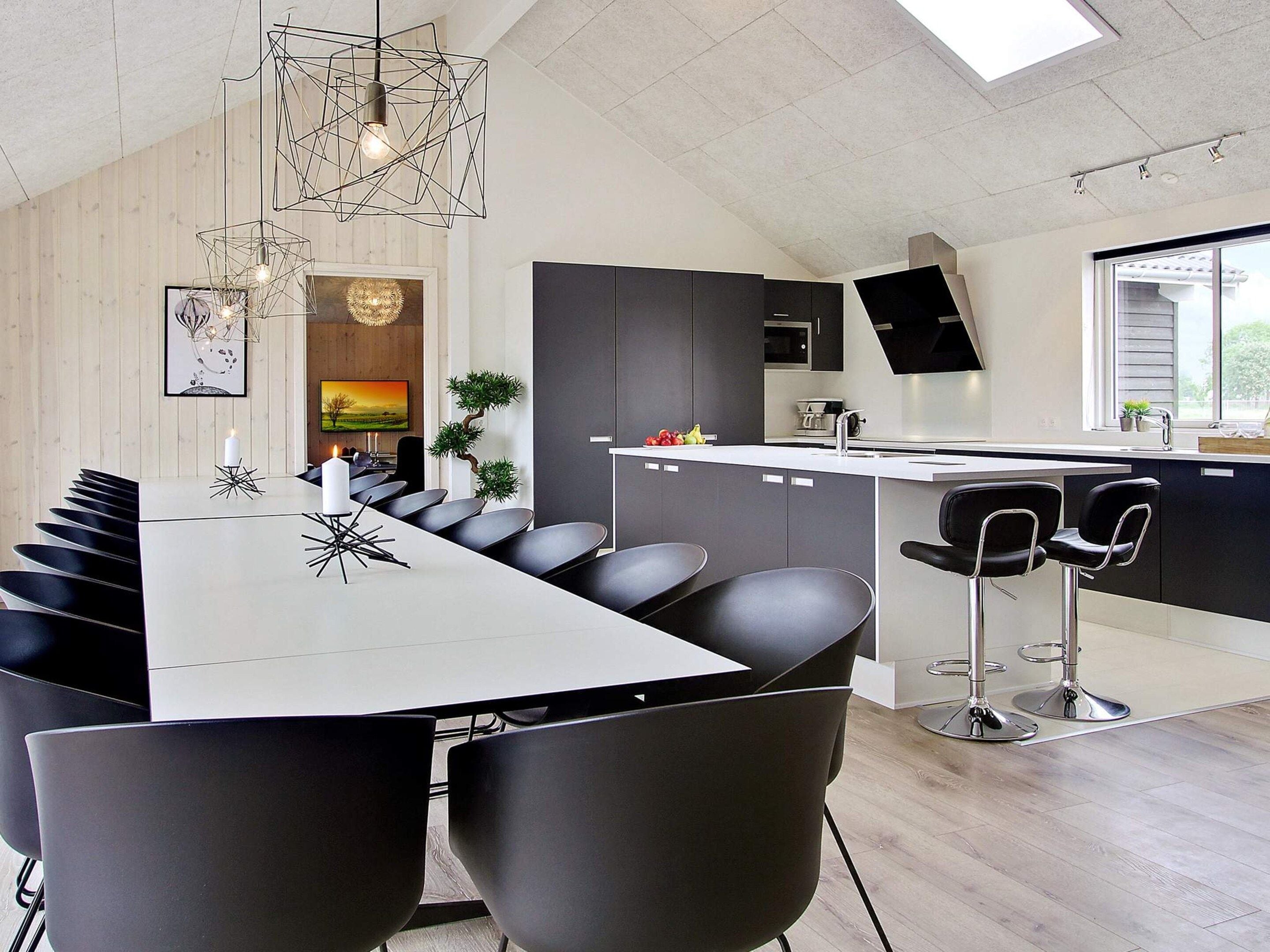 A modern kitchen with a central island, black bar stools, and a dining area with a long table and chairs.