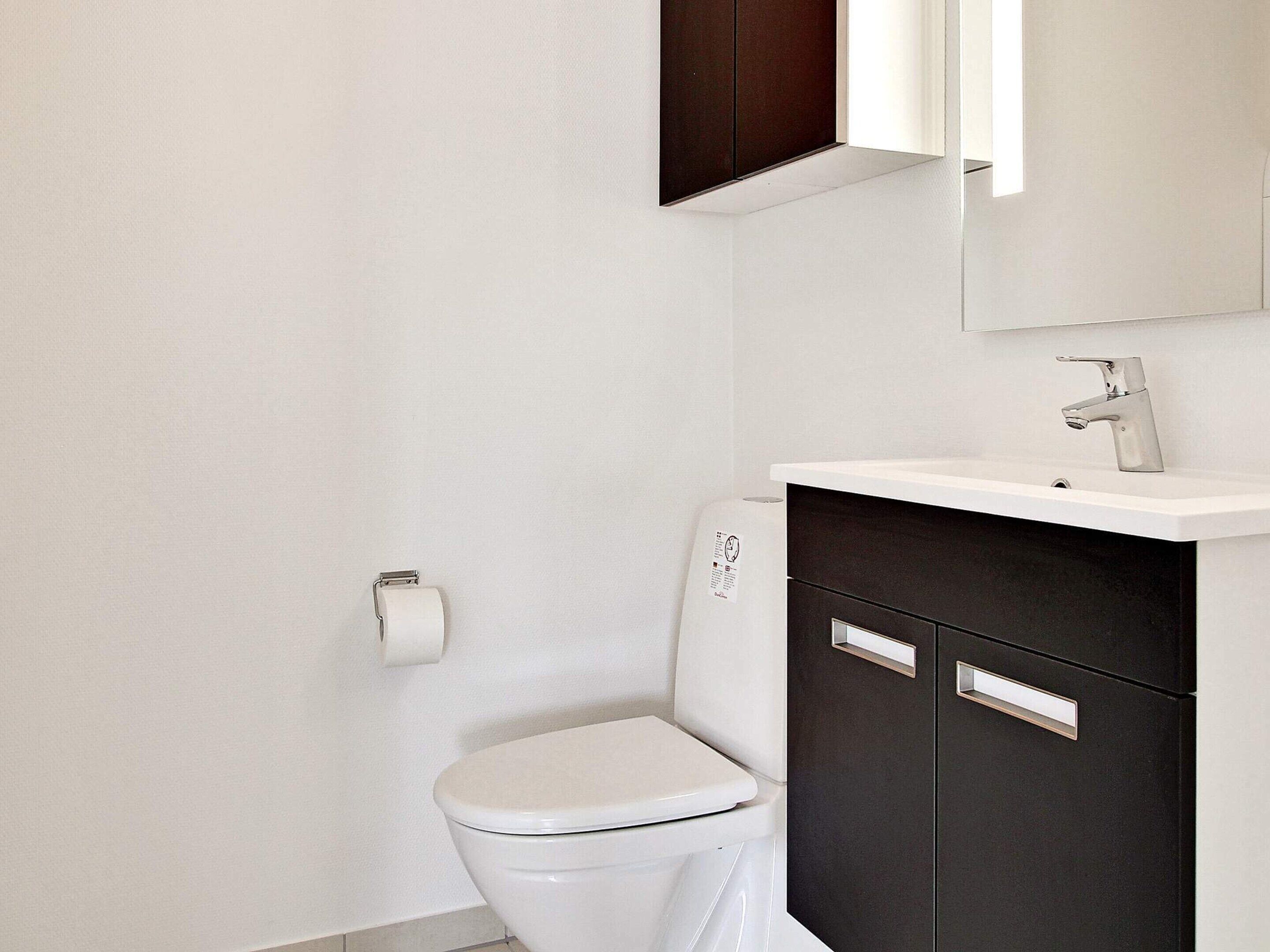 Ein Badezimmer mit einer weißen Toilette, einem dunklen Schrank und einem weißen Waschbecken mit Spiegel darüber.
