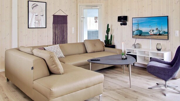 A modern living room with a beige sofa, a small coffee table, and a purple armchair. There is a television mounted on the wall, a cactus plant, and a framed picture on the wall. - Holiday Home in Kappeln (Kappeln)