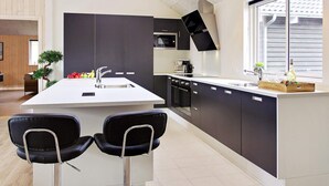 A modern kitchen with a central island, bar stools, a built-in oven, and a window providing natural light. - Holiday Home in Kappeln (Kappeln)