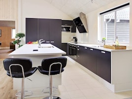 A modern kitchen with a central island, bar stools, a built-in oven, and a window providing natural light.