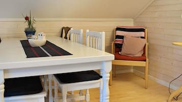 A dining area with a white table, black and red placemat, and a small boat decoration. There is a chair with a striped cushion and a plant on the table.