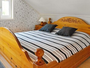 Una cama de madera con colcha a rayas y dos almohadas, una mesita de noche con lámpara y una ventana con papel tapiz floral.