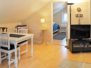 A cozy room with a dining table, chairs, a lamp, a television, and a bed in the background.
