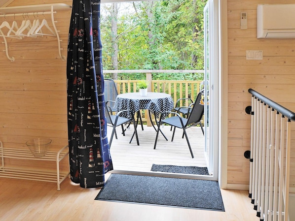 Una terraza de madera con mesa y sillas, vista a árboles, y una puerta que da a un espacio interior.