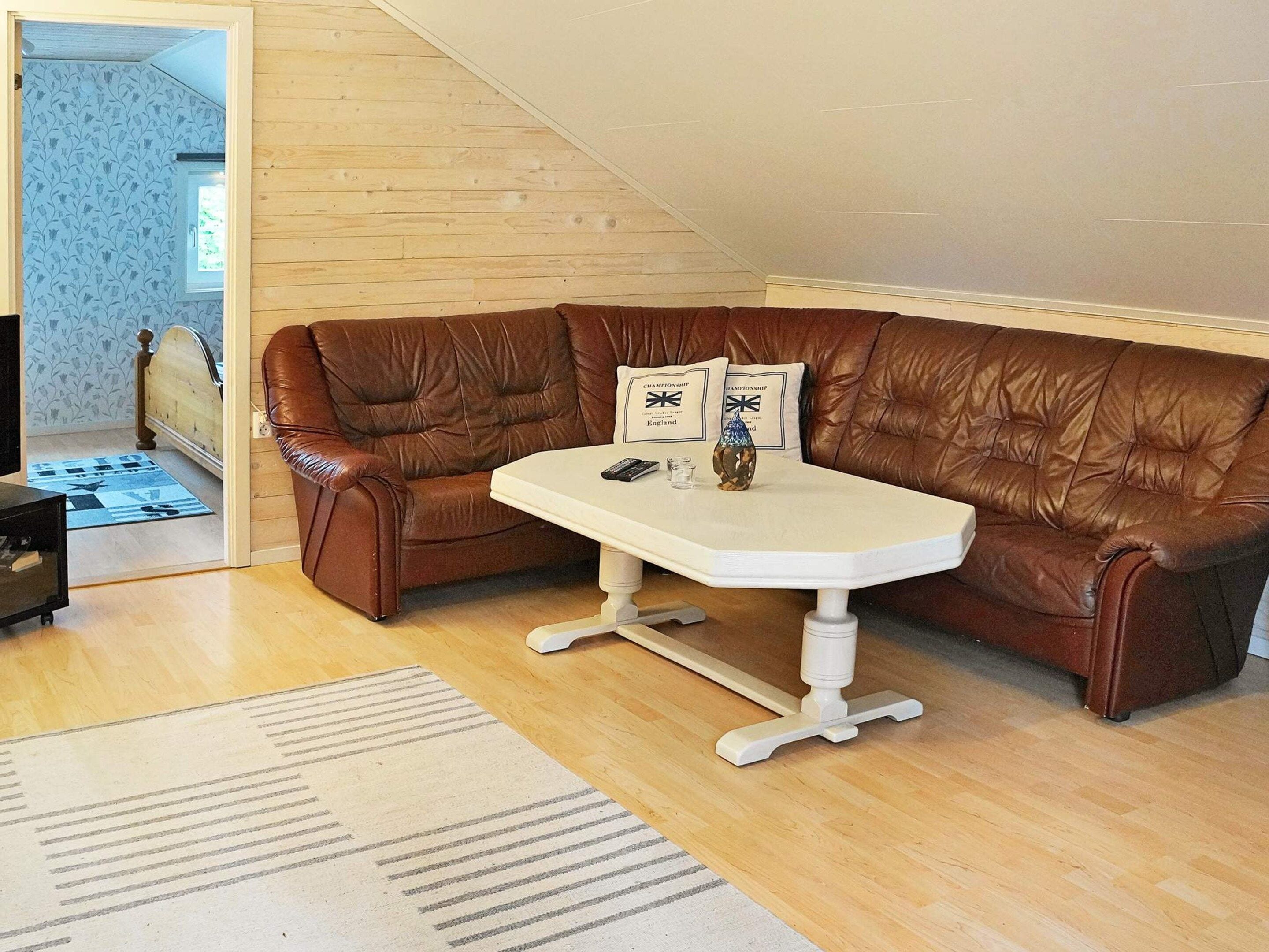 Un sofá de cuero marrón con una mesa blanca, una alfombra estampada y piso de madera.