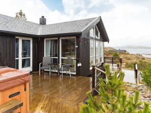 A wooden cabin with a deck, large windows, and a view of the ocean.
