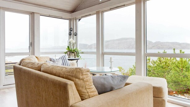 A modern living room with a beige sofa, a glass table, and a view of the sea through large windows.