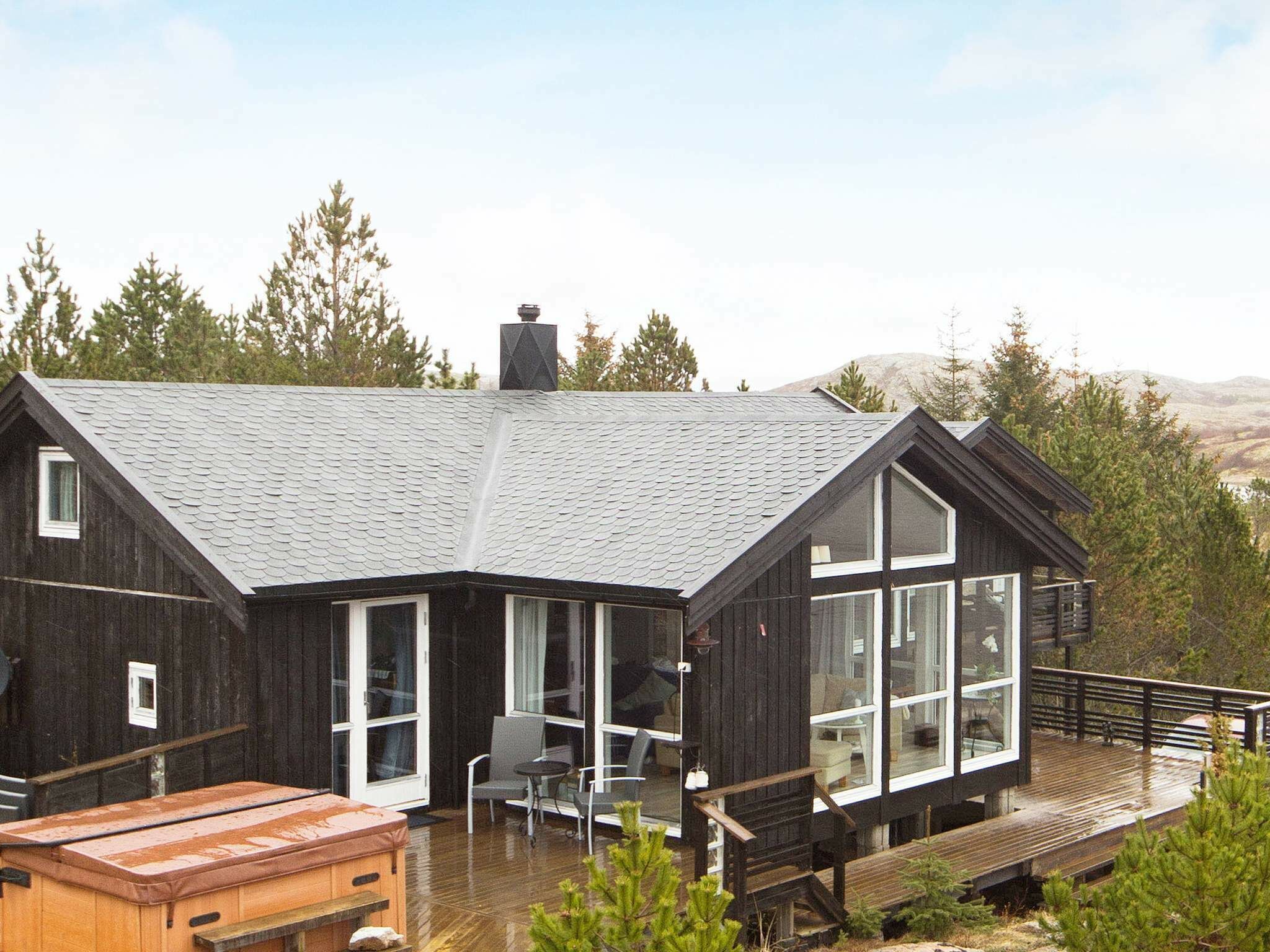 Une cabane moderne dotée d’un toit en pente, de grandes fenêtres et d’une terrasse en bois.
