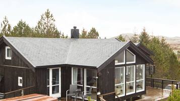 Une cabane moderne dotée d’un toit en pente, de grandes fenêtres et d’une terrasse en bois.