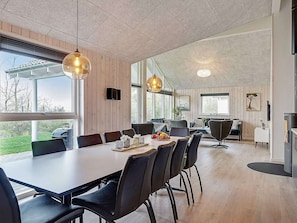Uma área de refeições moderna com uma mesa comprida, cadeiras pretas e iluminação pendente.
