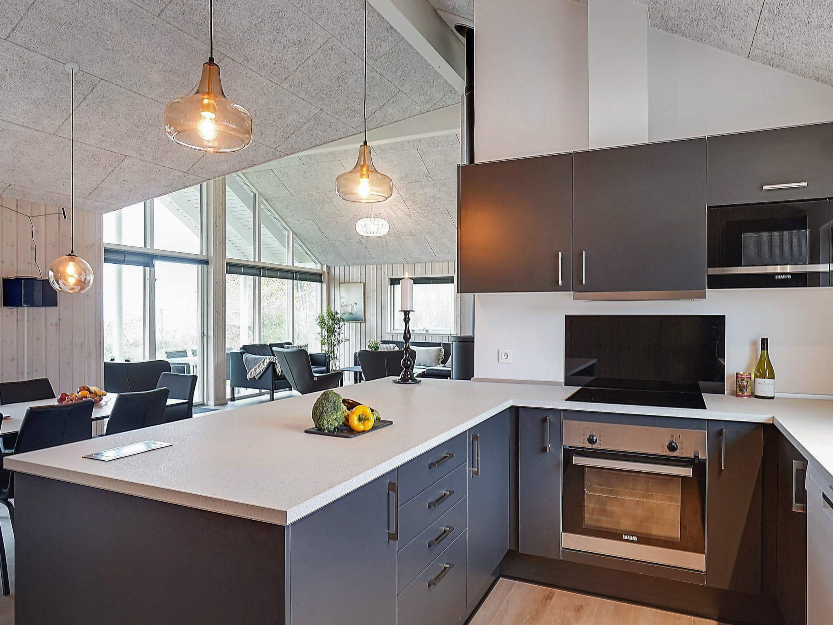 A modern kitchen with dark cabinets, a built-in oven, and pendant lighting.