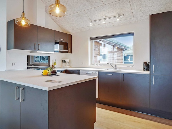 A modern kitchen with dark cabinetry, a large island, and pendant lighting.