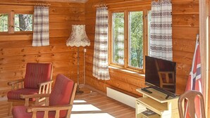 Een houten blokhutinterieur met een televisie, twee stoelen, een lamp en een klein houten kastje.