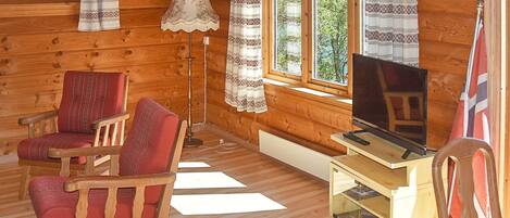 A wooden cabin interior with a television, two chairs, a lamp, and a small wooden cabinet.