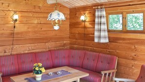 Interieur van een blokhut met een zithoek met houten bank, een tafel met een bloevas en twee wandlampen.