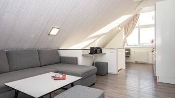 A modern loft apartment with a sloped ceiling, a grey sofa, a small table, and a kitchenette area.