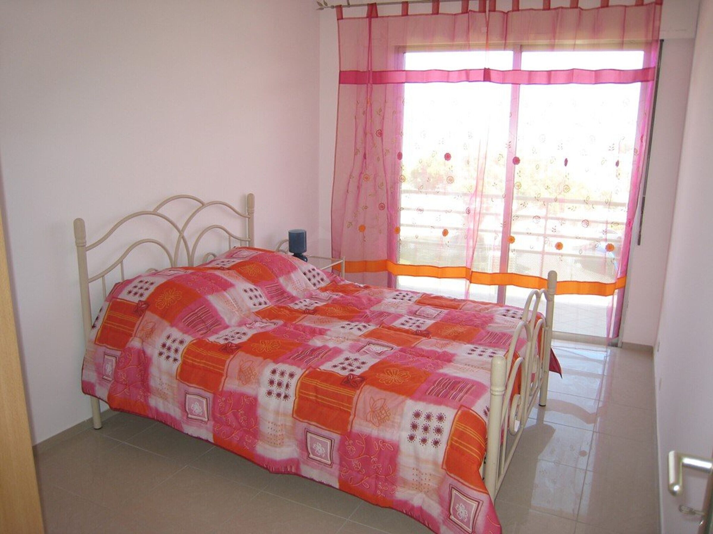 A bedroom with a bed, a window with curtains, and a door.
