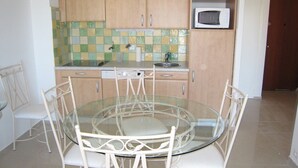 A small kitchen with a round glass table and white chairs, wooden cabinets, a microwave, and a tiled backsplash. - Central 2BR with Balcony & A/C - 3rd Floor - Cavalaire-sur-Mer (Cavalaire-sur-Mer)