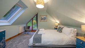 Quarto com claraboia, cama com lençóis brancos, manta cinza e mesa de cabeceira com abajur.
