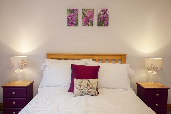 A neatly made bed with white linens and two decorative pillows, flanked by two nightstands with lamps and a wooden headboard.