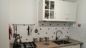 A kitchen with white cabinets, a gas stove, a sink, and various kitchen utensils.