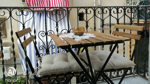 A balcony with a wooden table and chairs, a striped cloth, and an air conditioning unit.