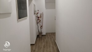 A narrow hallway with white walls, a potted plant with red flowers, and a framed picture on the left.