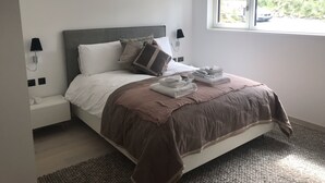 A neatly made bed with a brown blanket, white pillows, and a view of greenery outside the window. - Red Stag With Stunning Loch and Waterfall View (Crianlarich)