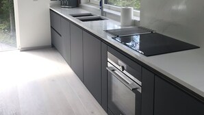 A modern kitchen with a black countertop, a window, and a view of trees. - Red Stag With Stunning Loch and Waterfall View (Crianlarich)