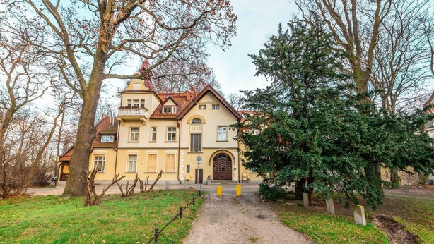 A historic building with a central entrance, surrounded by trees and a gravel path. - Victus Apartamenty - Bolek (Sopot)
