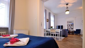 A hotel room with a bed, a desk, a chair, a sofa, and a bookshelf. - Victus Apartamenty - Bolek (Sopot)