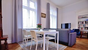 A living room with a white table, chairs, a grey sofa, a TV, and a bookshelf. - Victus Apartamenty - Bolek (Sopot)