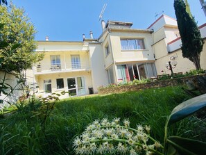 A two-story building with a balcony and a garden area with flowers and grass. - Reims Sherpa Guest House (Reims)