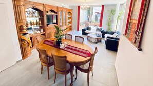 Un vaste espace de vie comprenant une table à manger, des chaises et un canapé. On y trouve également un téléviseur et un meuble contenant des objets décoratifs.
