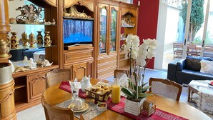 Un coin repas avec une table en bois dressée pour le repas, entourée de meubles en bois richement décorés et d’un téléviseur diffusant une scène de forêt enneigée.