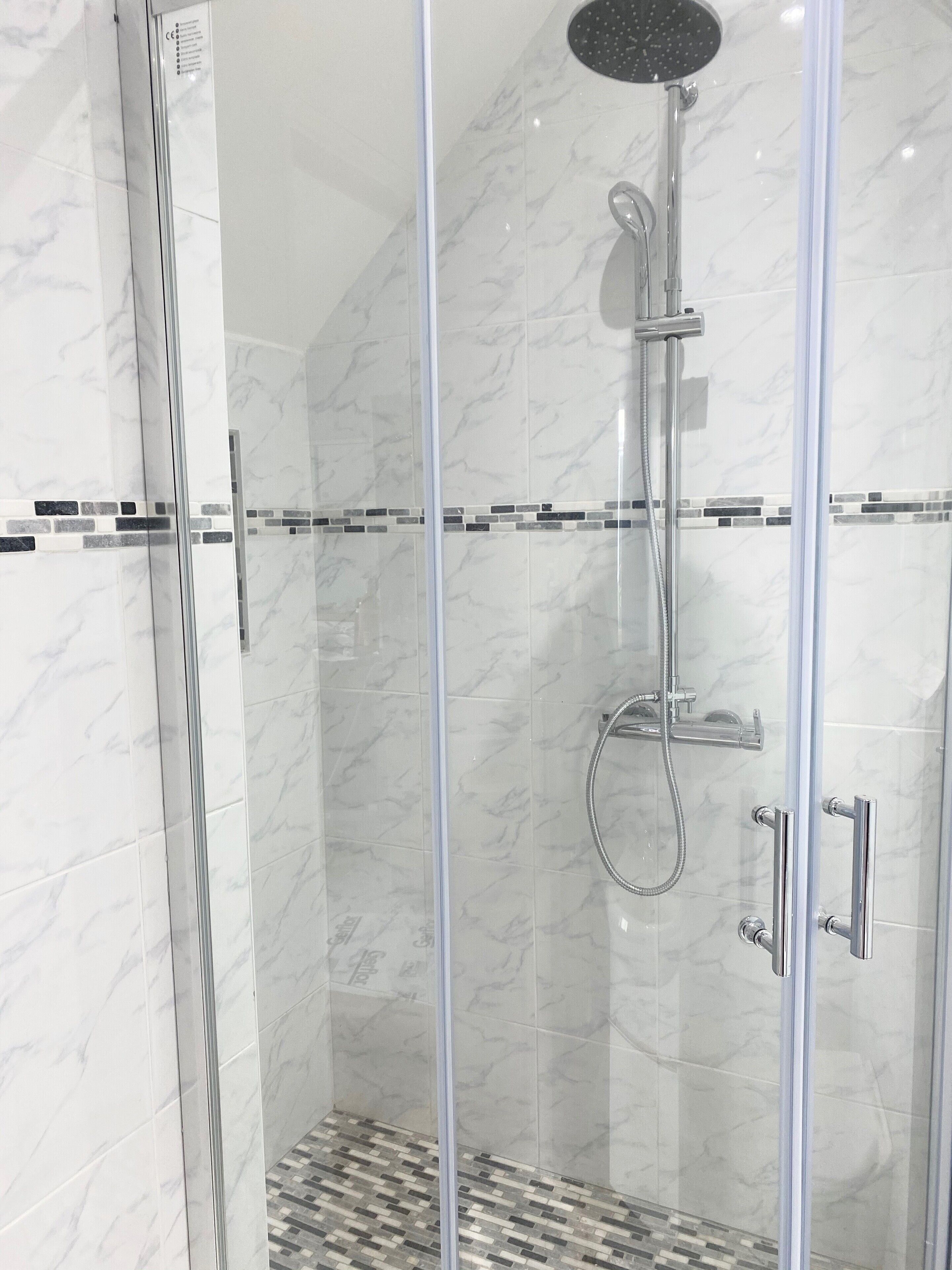 A glass-enclosed shower with a handheld showerhead and a wall-mounted faucet.