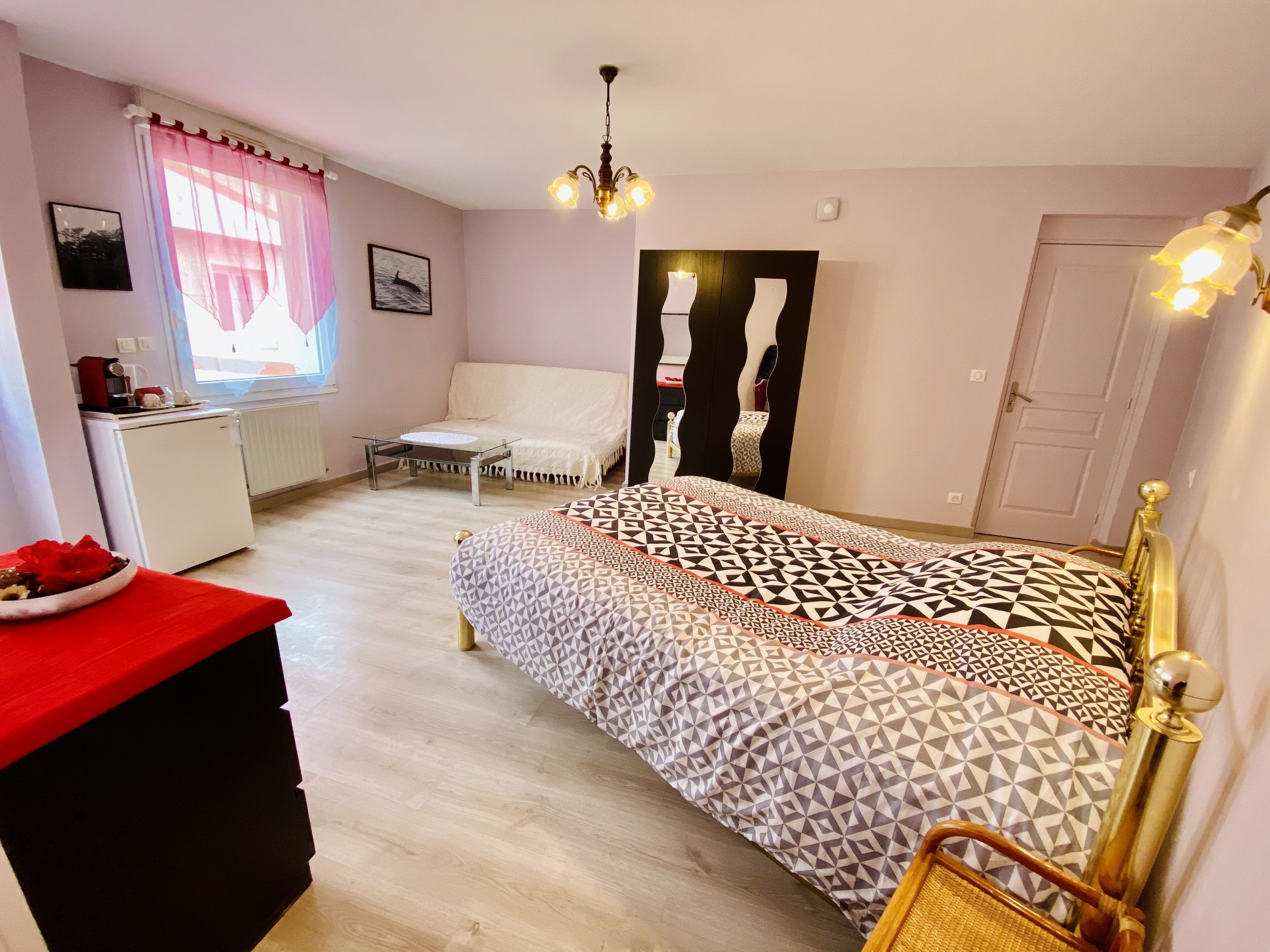 Een slaapkamer met een bed, een bureau, een stoel, een bank en een raam met gordijnen.