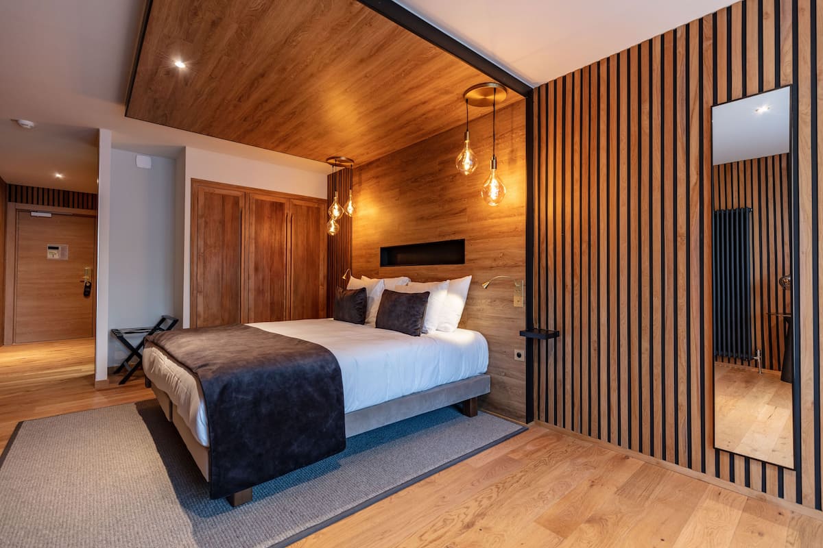 A modern bedroom with a wooden ceiling, a bed with a dark headboard, and a large mirror on the wall.