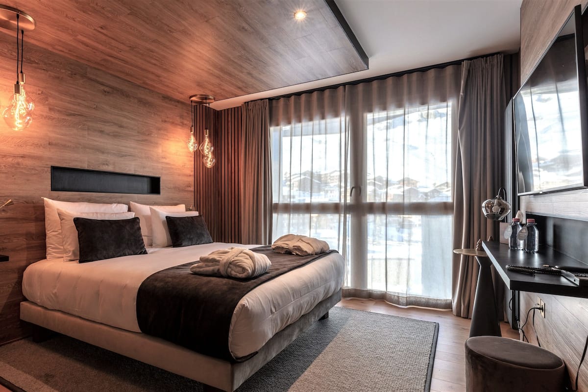 A modern hotel room with a large bed, bedside lamps, a desk with a computer, and a view of the outside.