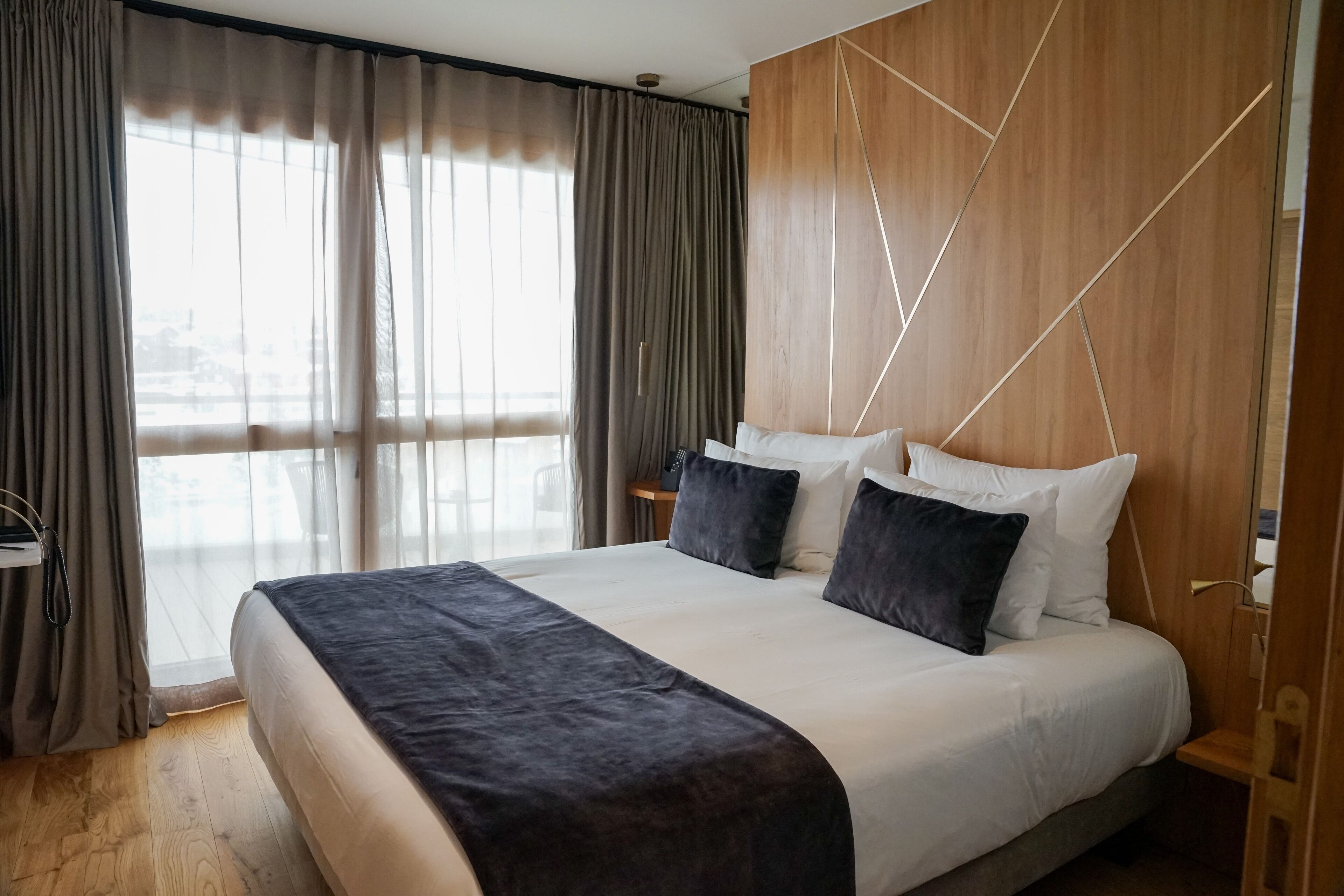 Habitación de hotel moderna con una cama grande, cabecero de madera y vistas al exterior.