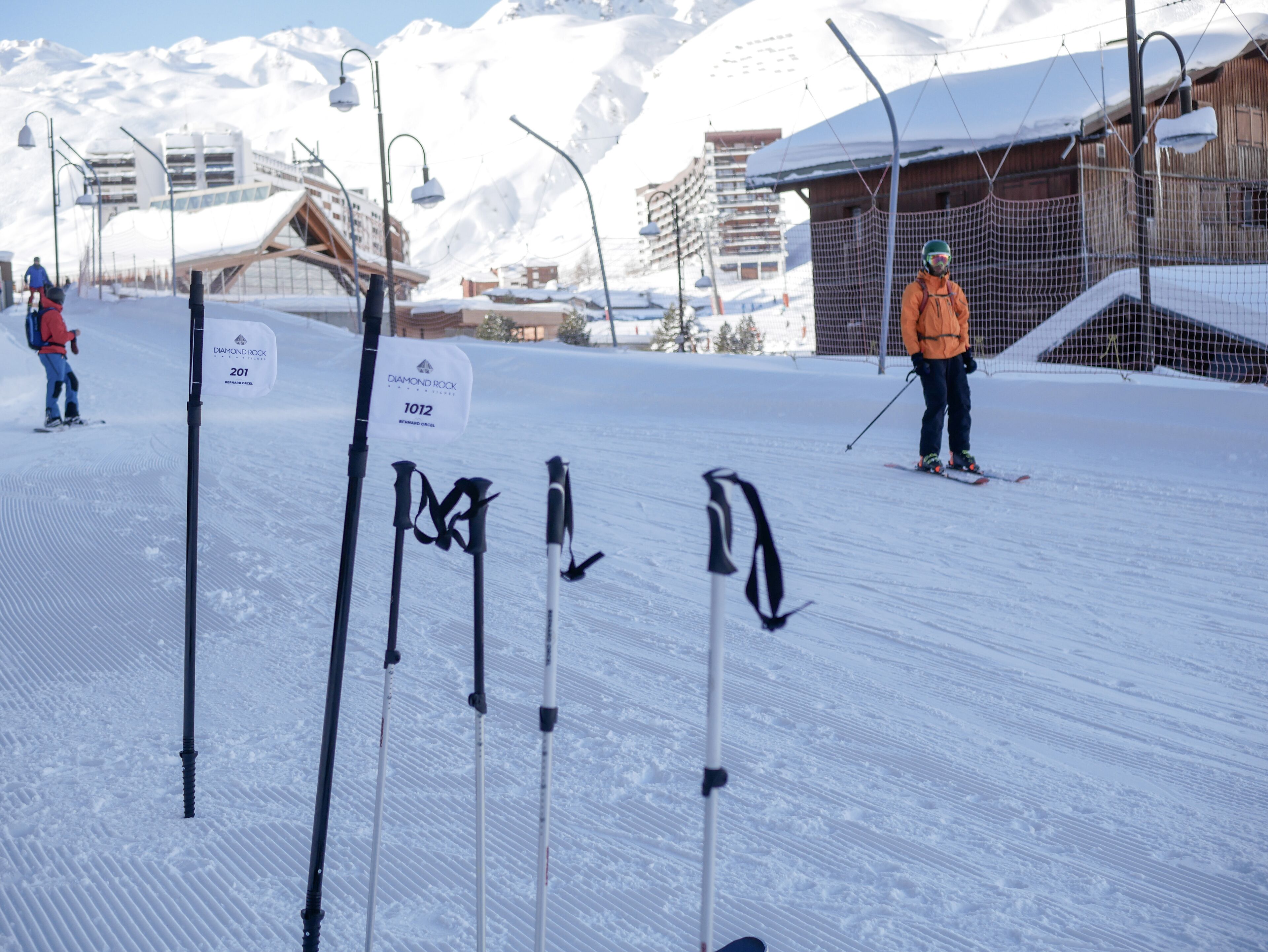 A ski slope with marked ski runs, a person skiing, and a wooden building in the background.