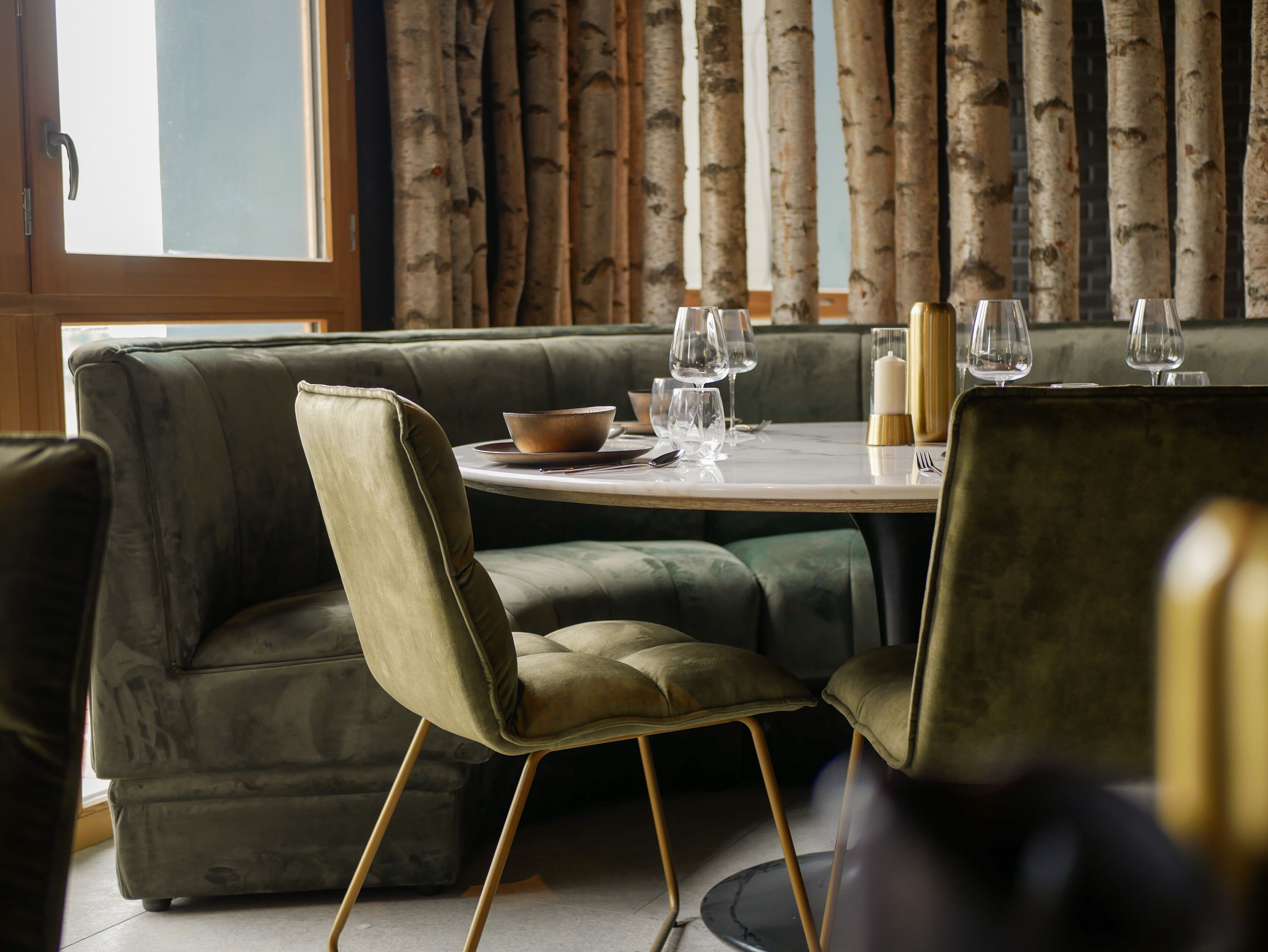 A dining area with a round table set for four, surrounded by a green velvet sofa and matching chairs.
