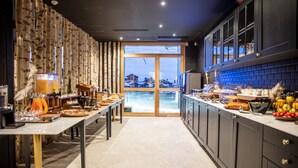 Une cuisine moderne dotée d’un long comptoir, d’un coin repas et offrant une vue sur un paysage enneigé grâce à de grandes fenêtres.