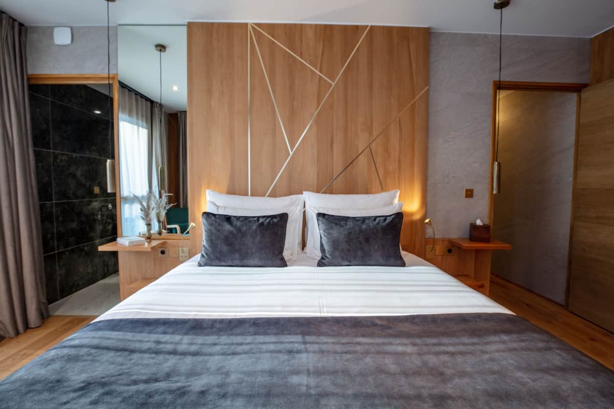 A modern bedroom with a large bed, wooden headboard, and a nightstand with a lamp.