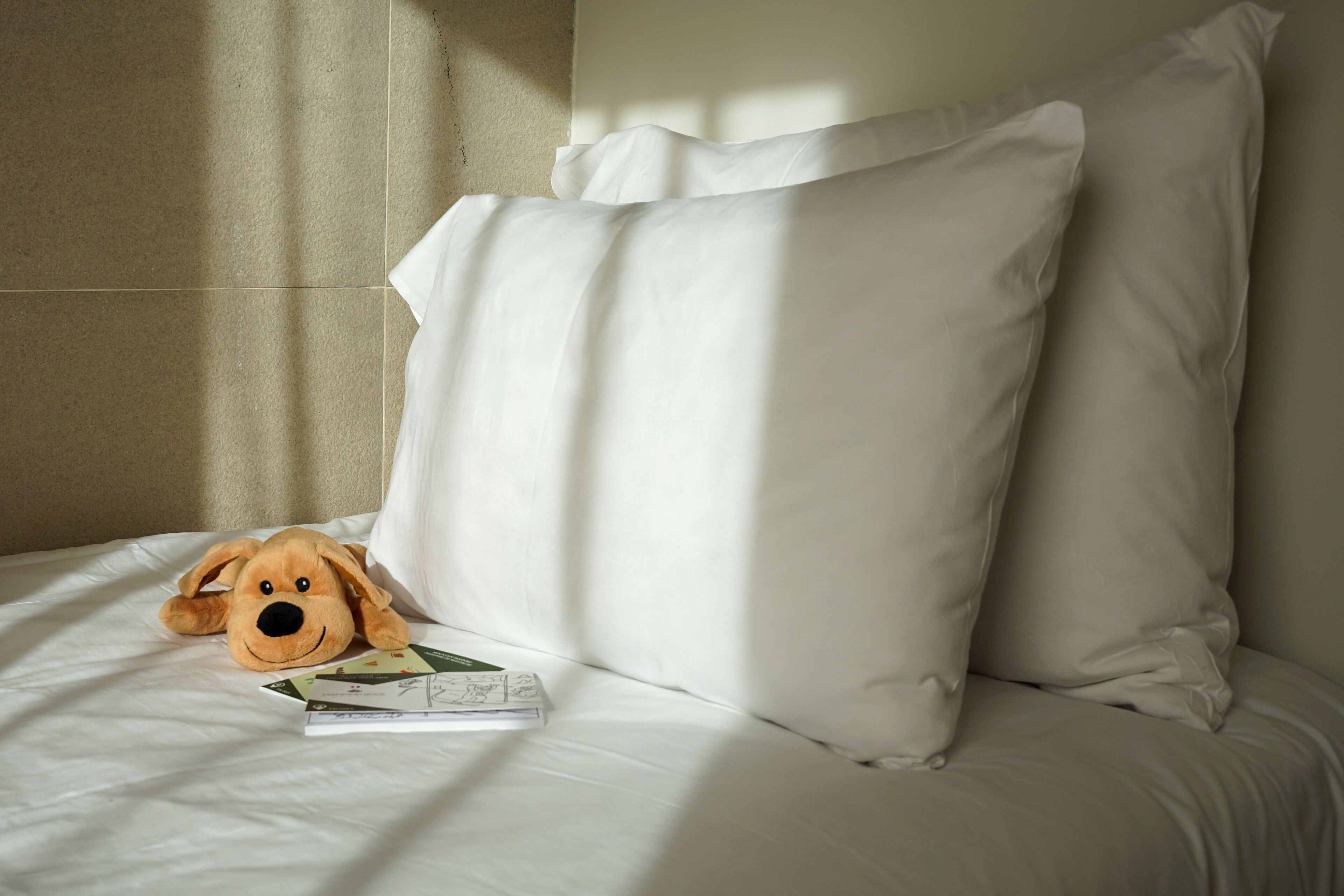 A bed with white bedding and a stuffed dog toy.