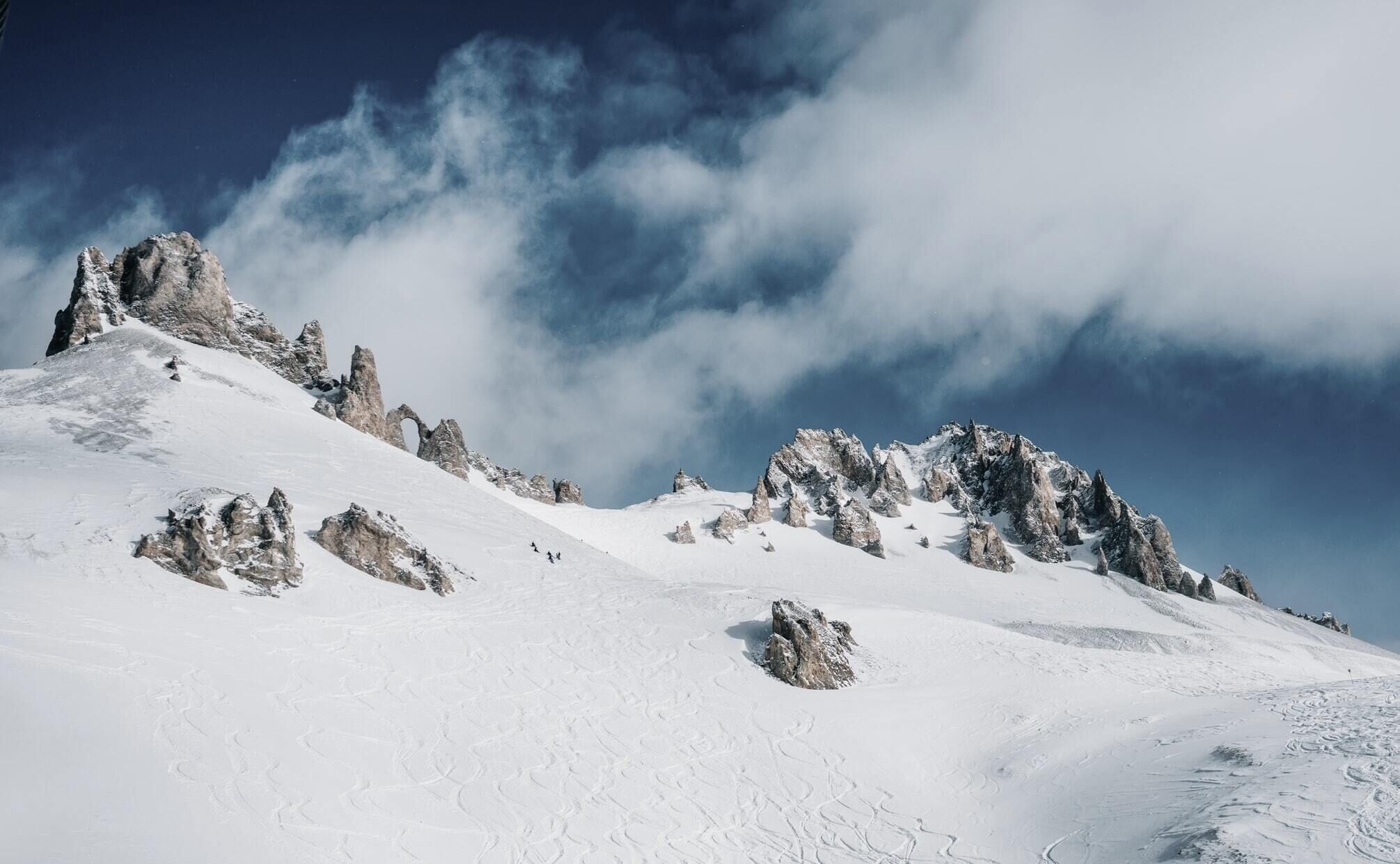 A snow-covered mountain with rocky outcrops and a clear sky.
